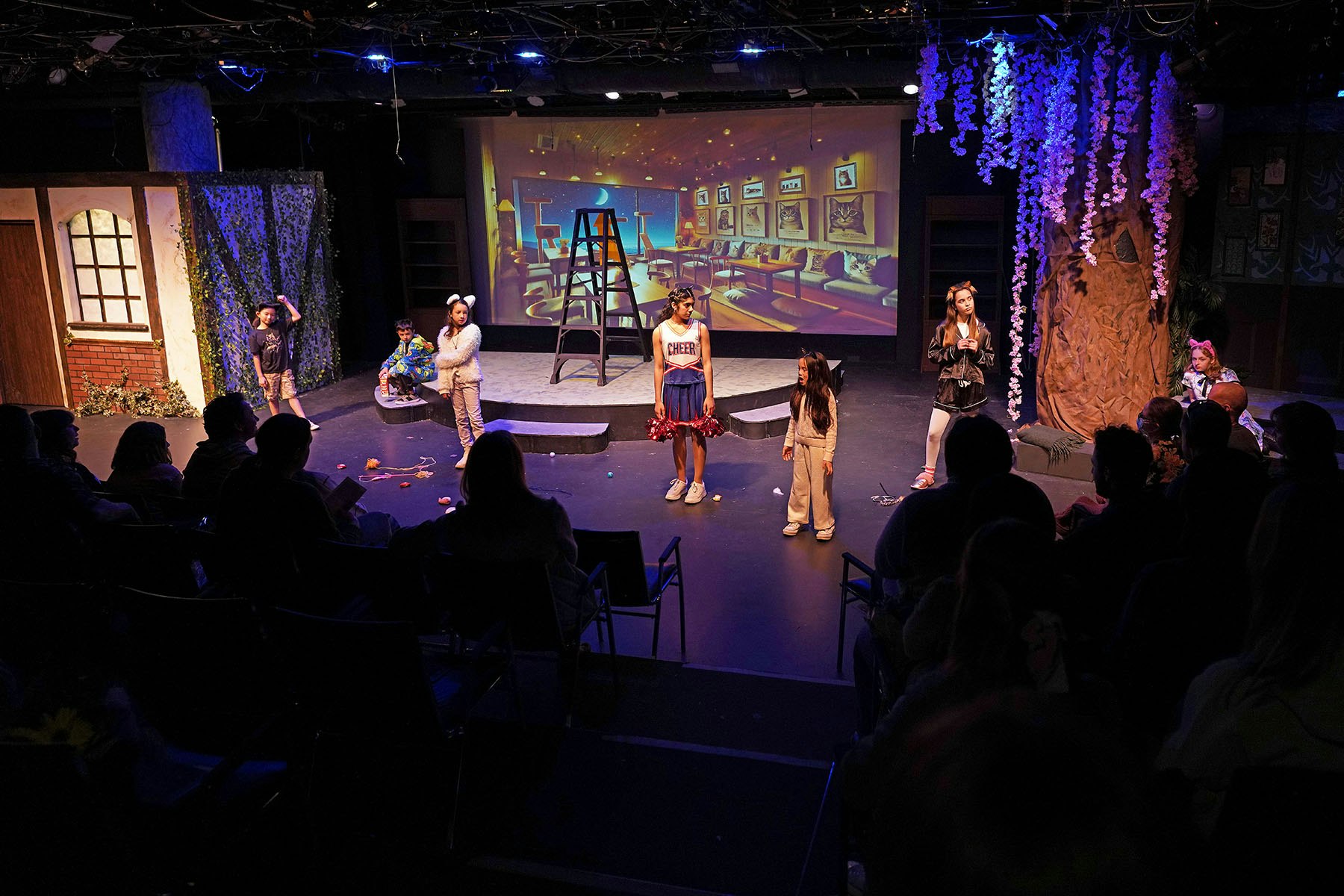 A theater stage with young actors performing a play in front of an audience.