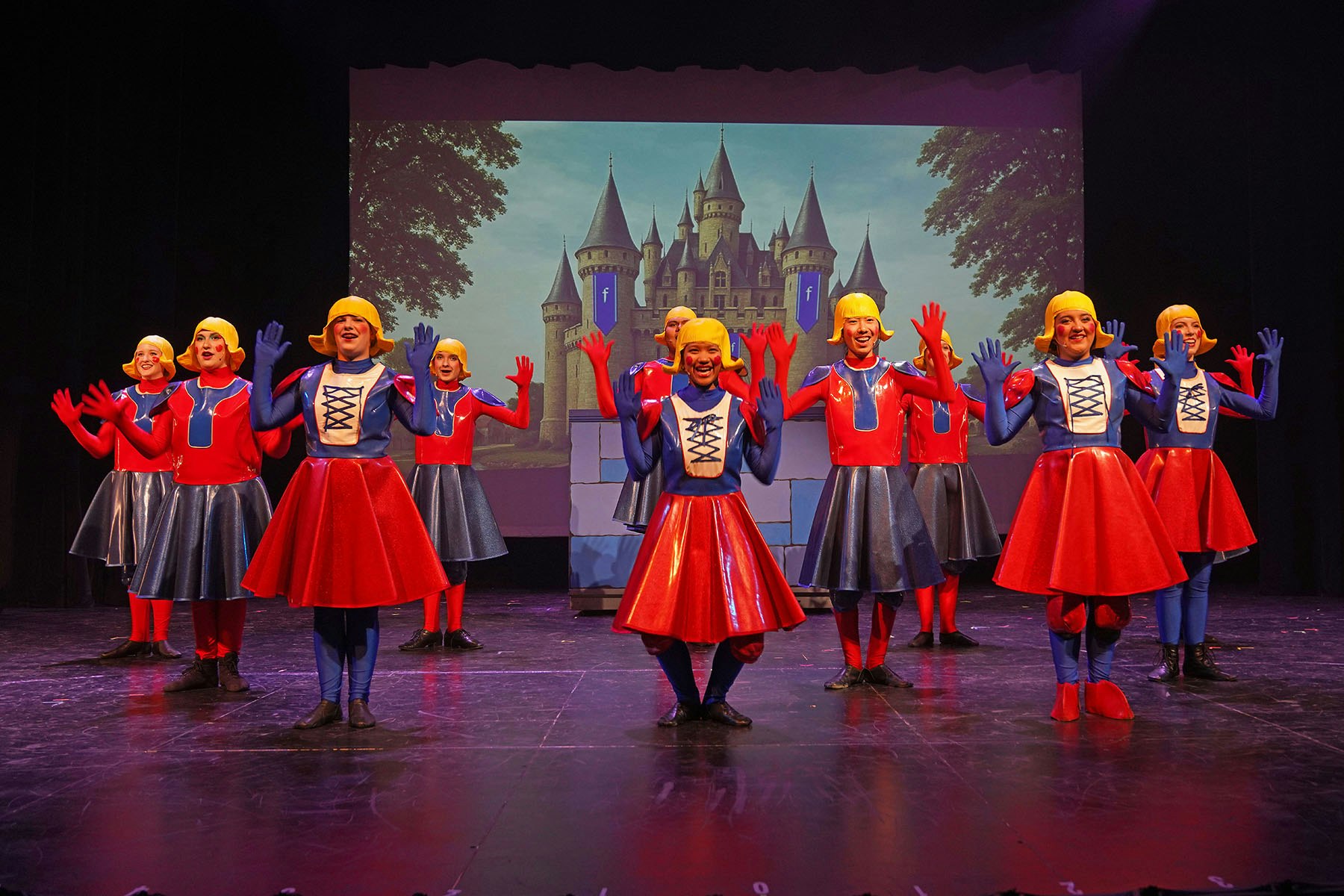 Performers in colorful costumes on stage, with a castle backdrop.