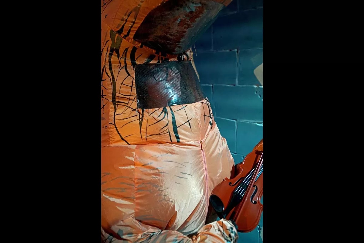 A person in an inflatable dinosaur costume holding a violin.