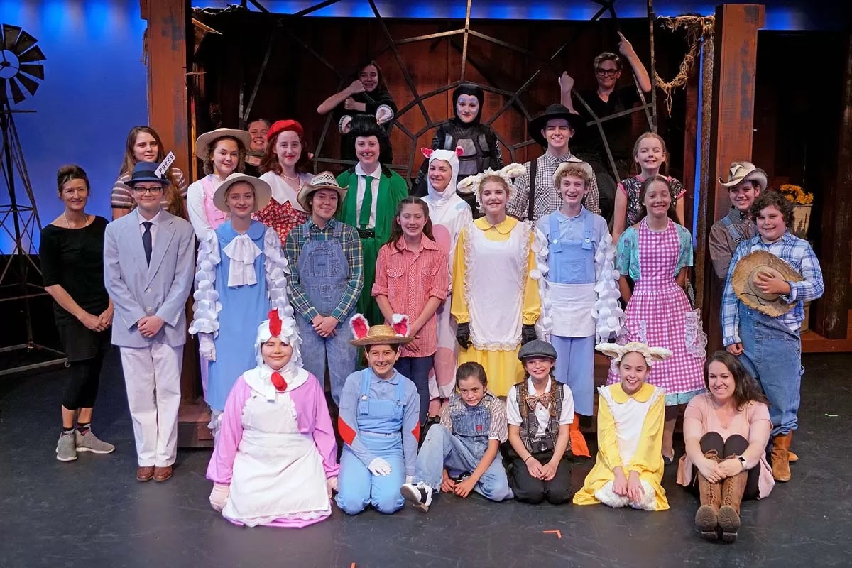 A group of people in colorful costumes posing on a stage set, likely a theater cast.