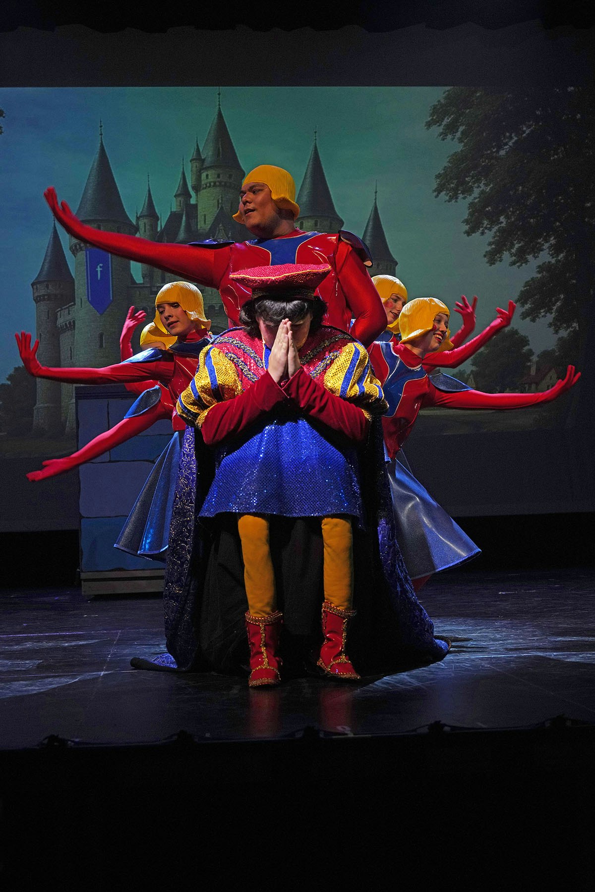 Performers in colorful costumes on stage, with a castle backdrop.