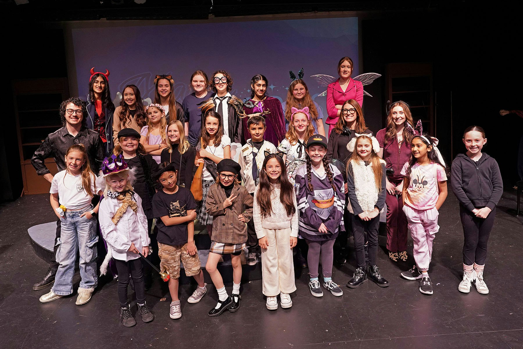 A group of children and adults in various costumes posing on a stage.