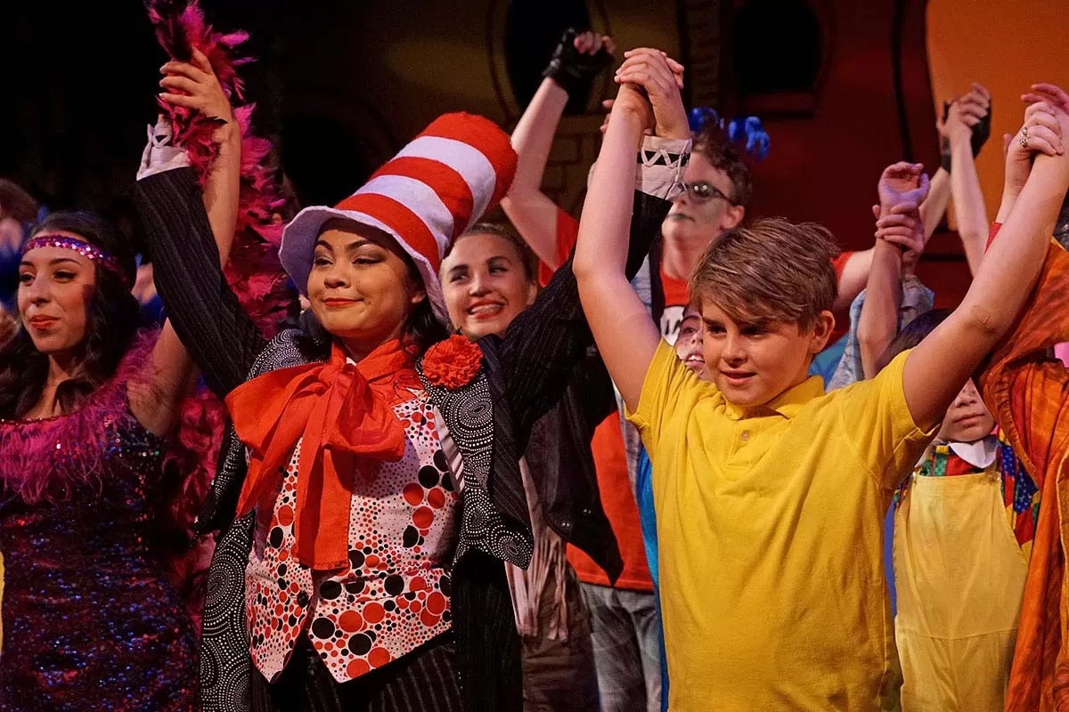 A group of people in colorful costumes, raising their hands, possibly at the end of a performance.