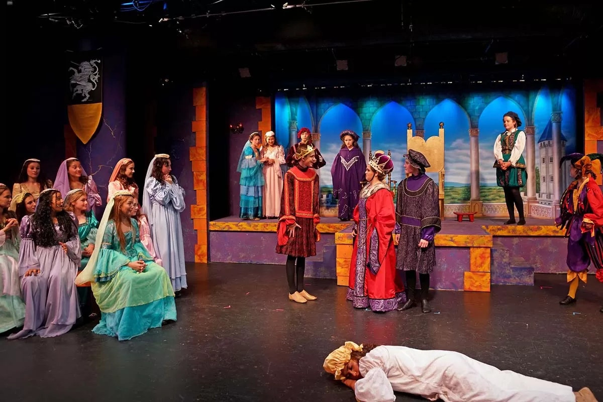 A theatrical play with a medieval setting, featuring actors in colorful costumes on stage.