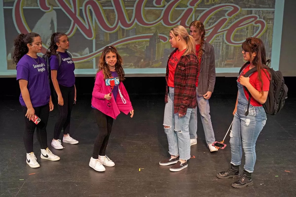 A group on stage, two in red shirts, three in purple, one holding a selfie stick. Background reads "Chicago."