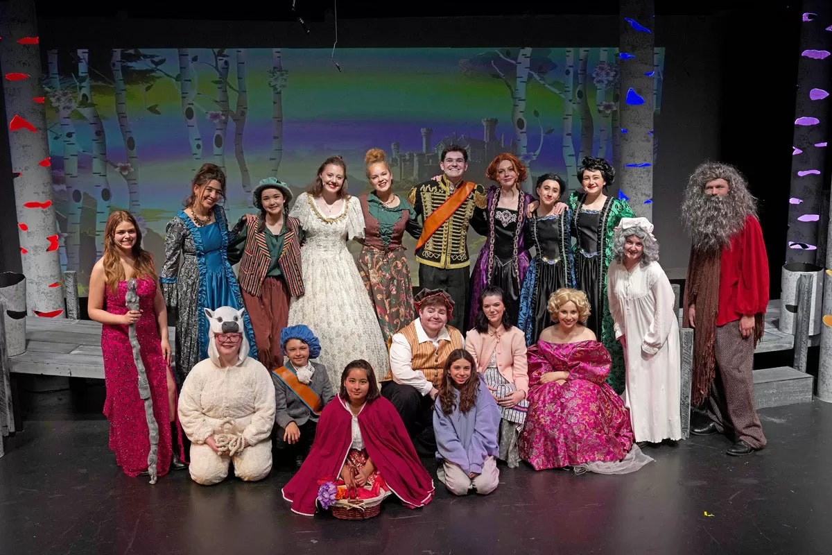 A group of people in colorful costumes posing on a stage, likely part of a theatrical production.