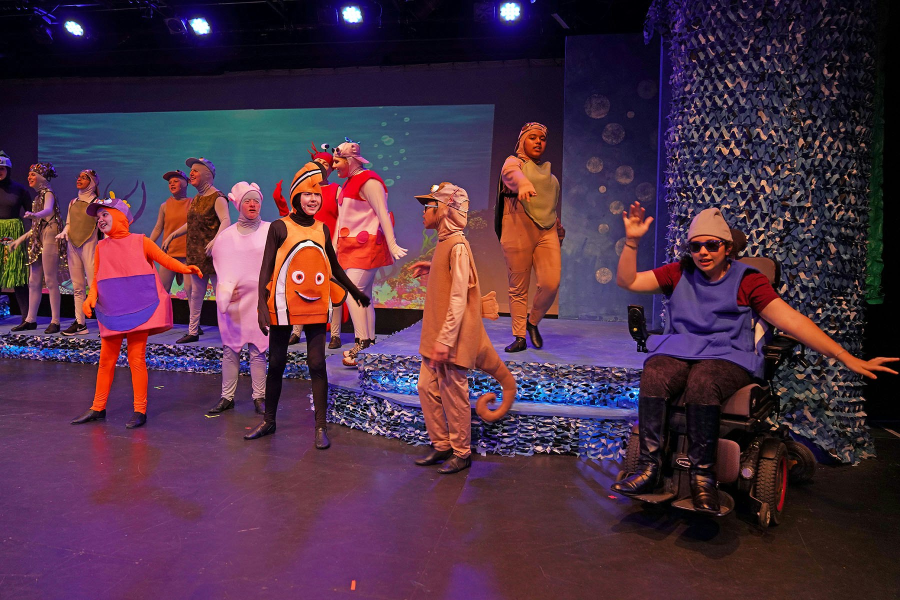 A group of people in colorful ocean-themed costumes performing on stage.