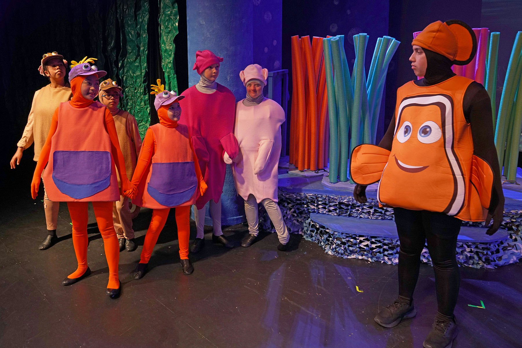 People in colorful underwater-themed costumes on stage, resembling fish and ocean creatures.