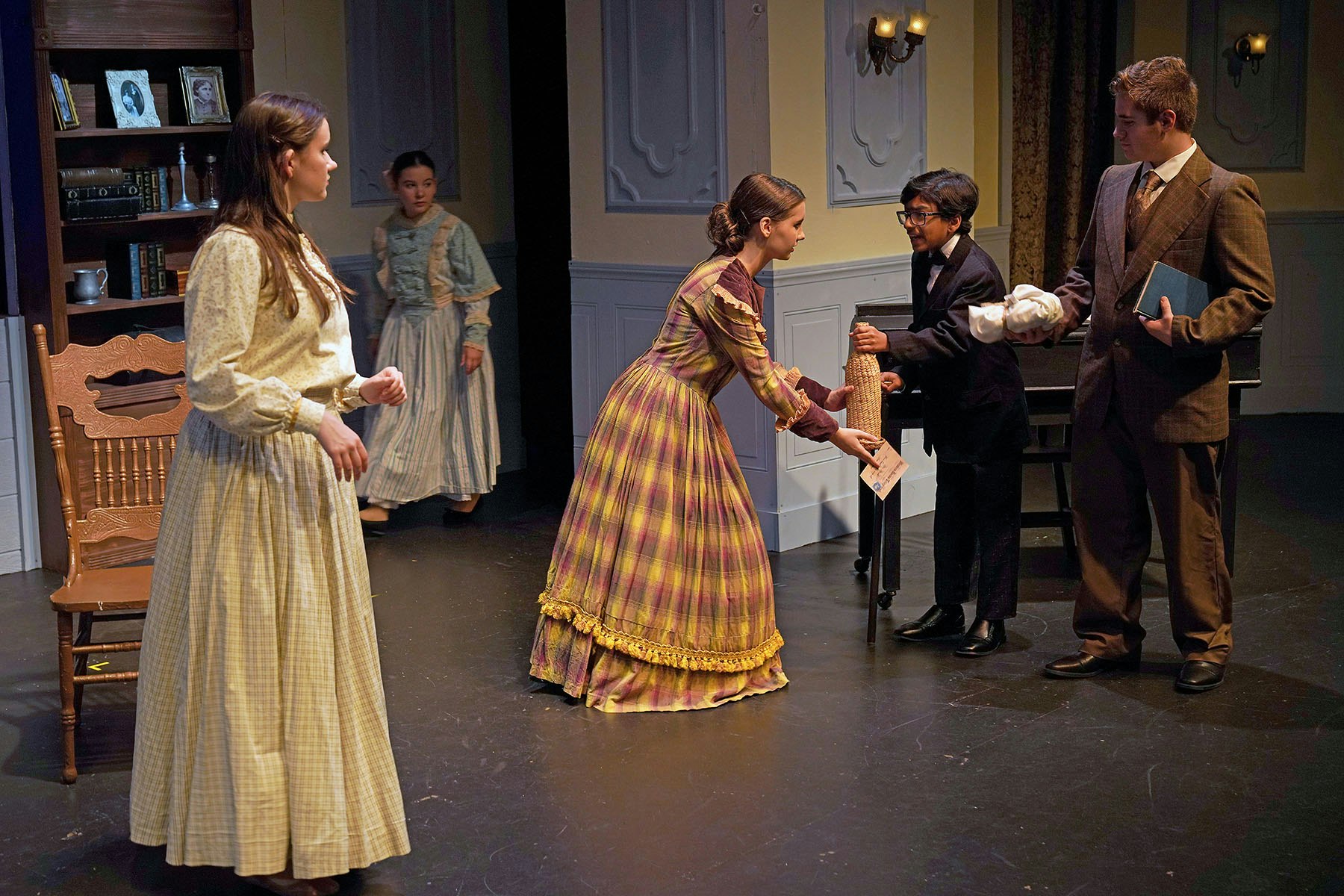 A theatrical scene with four actors in period costumes, engaged in a dialogue, suggesting a moment of exchange or interaction.