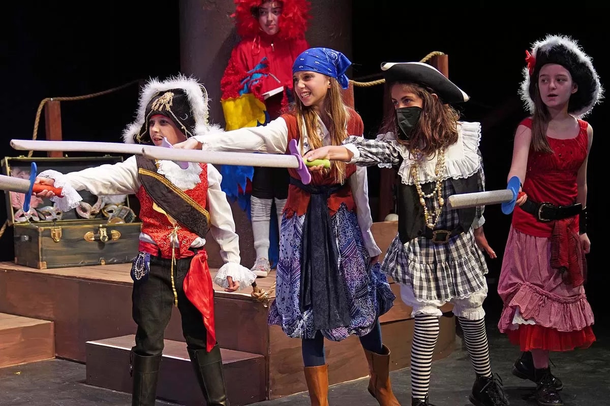 Children dressed as pirates with toy swords, performing on stage.