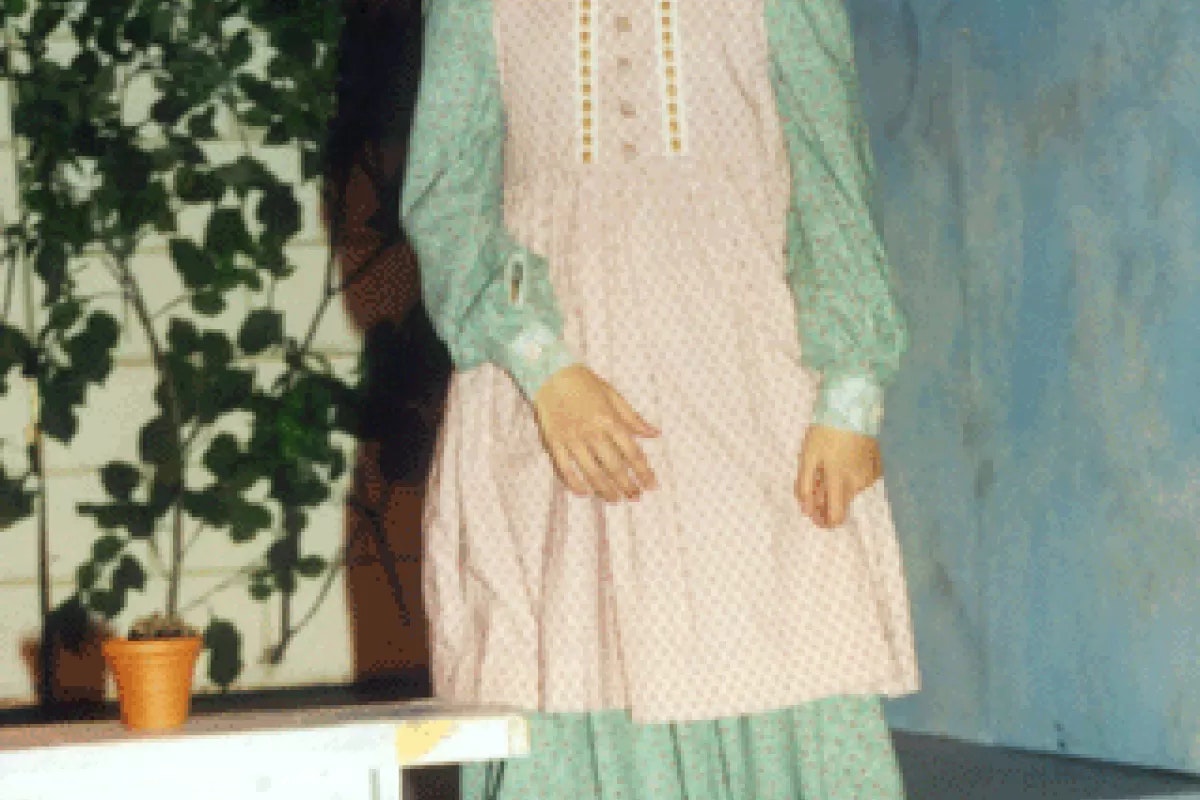 A person in vintage-style clothing stands near a small plant pot and foliage in the background.
