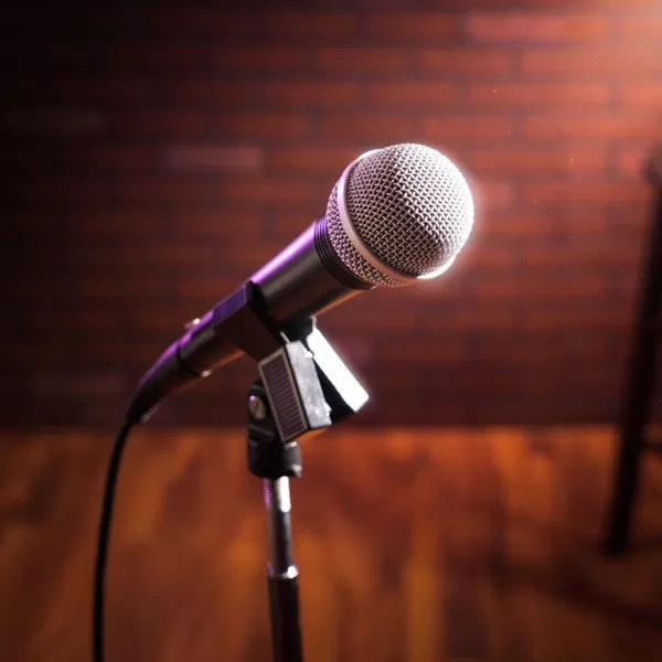 A microphone on a stand, in front of a blurred brick wall background.