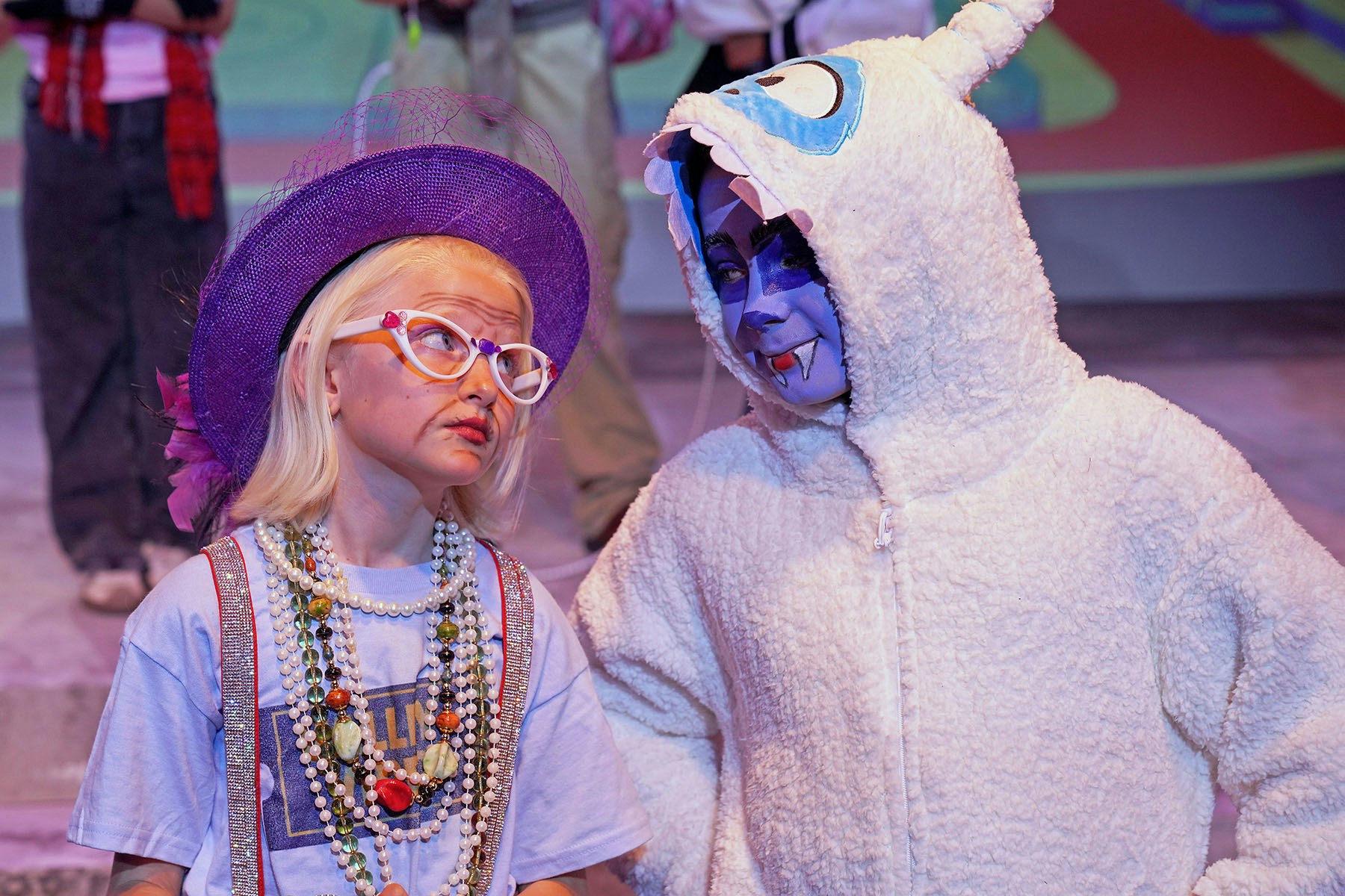 The image shows two children in costumes: one wearing a purple hat and glasses, and the other in a fluffy white outfit with face paint.