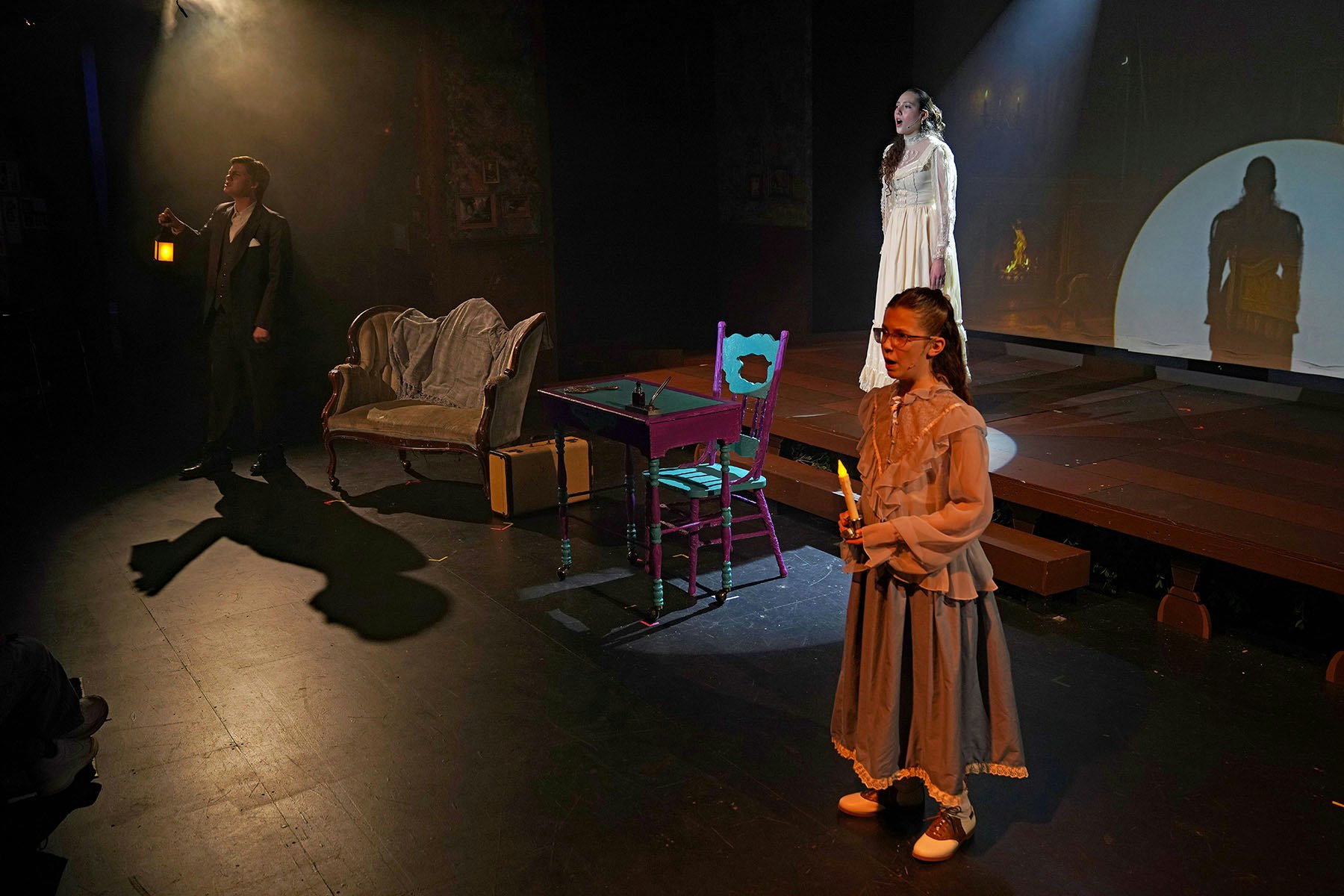 A theatrical performance with three actors on stage, vintage furniture, and dramatic lighting.