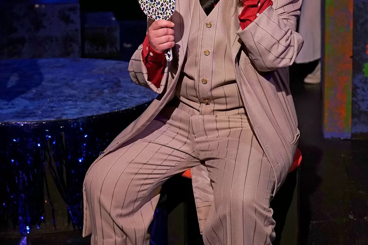 Person in a pinstripe suit sitting down, holding a small leopard-print mirror.
