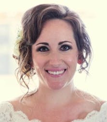 A woman smiling, wearing wedding attire with curled hair and a floral hairpiece.