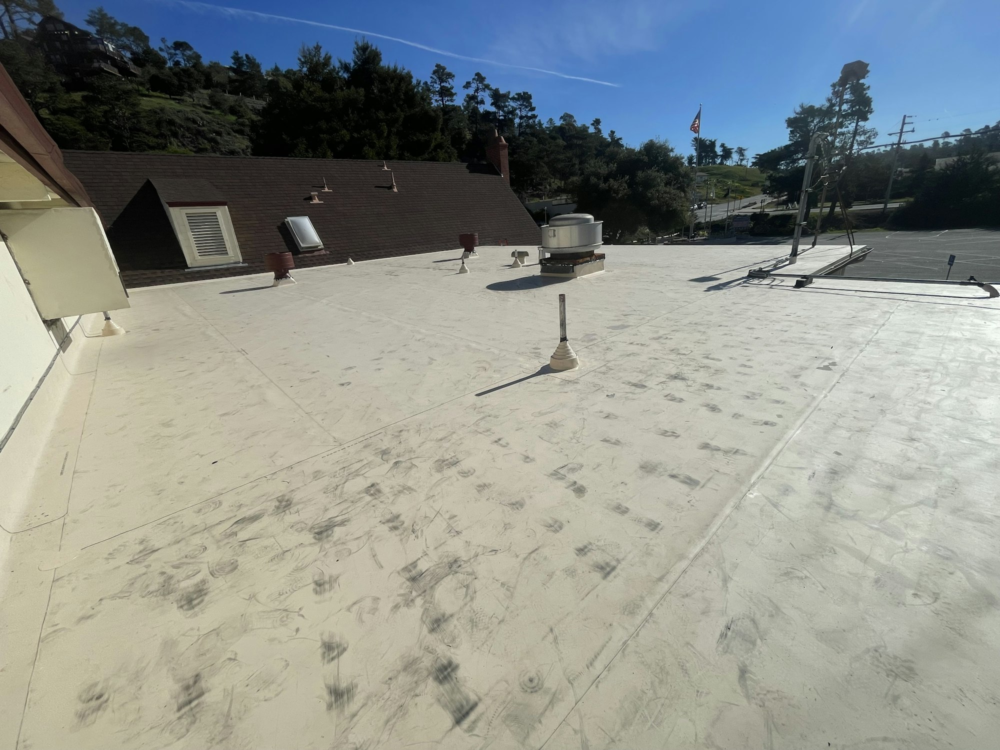 A flat rooftop with HVAC units and vents, overlooking a green hillside and a clear blue sky.