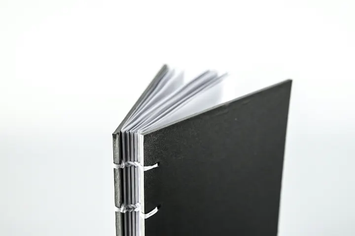 A close-up of a black, hardcover book with white pages and a visible binding.
