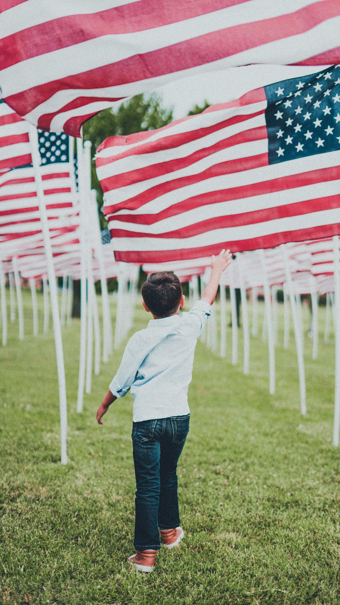 May contain: clothing, pants, grass, plant, flag, photography, american flag, face, head, person, portrait, boy, child, male, jeans, architecture, building, outdoors, and shelter