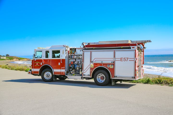 A red fire truck parked by a coastal road with ocean and blue sky in the background.