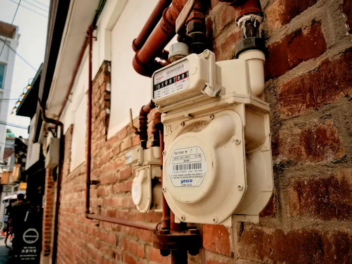 A utility meter on a brick wall with pipes.