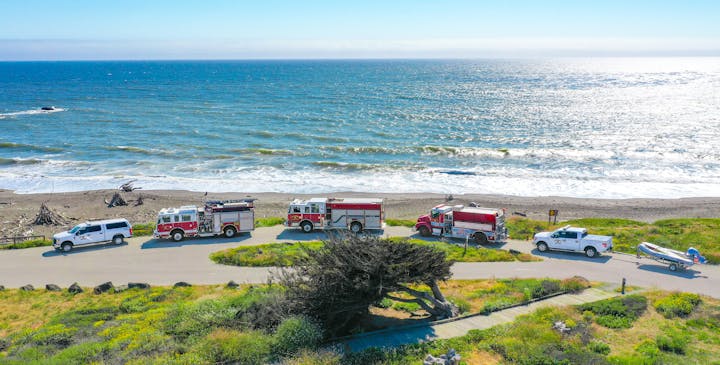 Emergency vehicles parked along a coastal road with the ocean in the background.