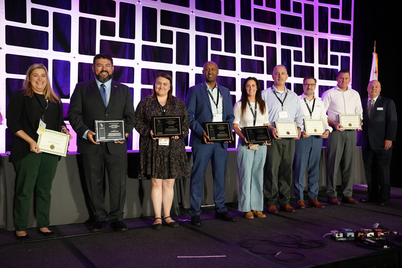 A group of people on stage holding awards, posing for a photo with a geometric backdrop.