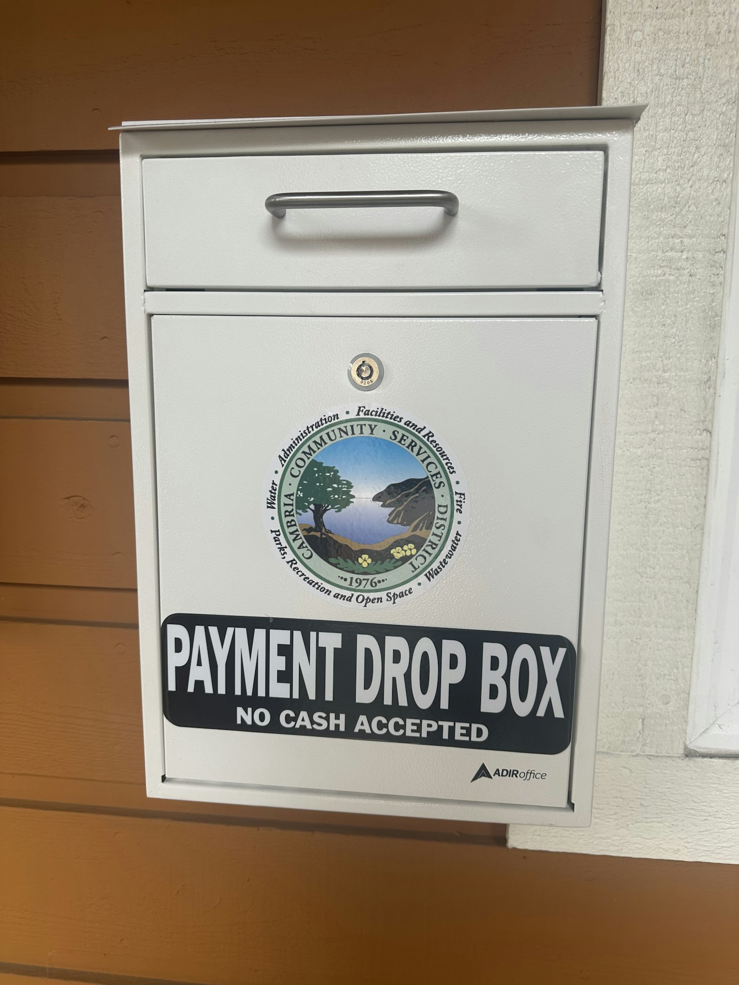 White payment drop box labeled "No Cash Accepted" with a community services district seal.