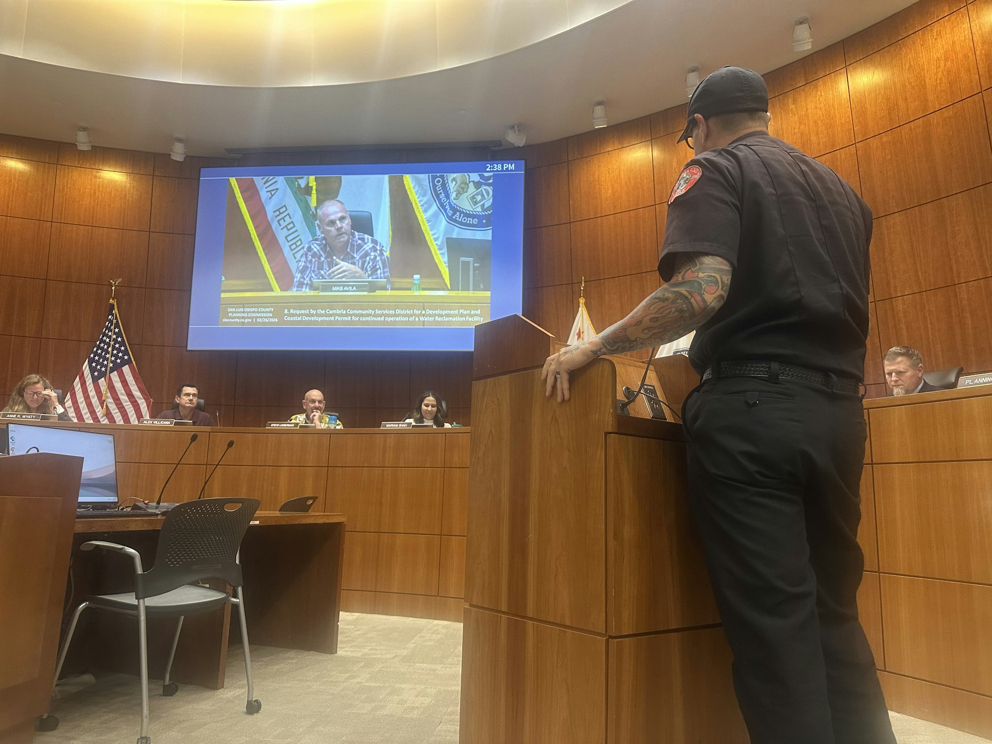 A public meeting where a speaker addresses officials about a water reclamation facility, with audience members present.