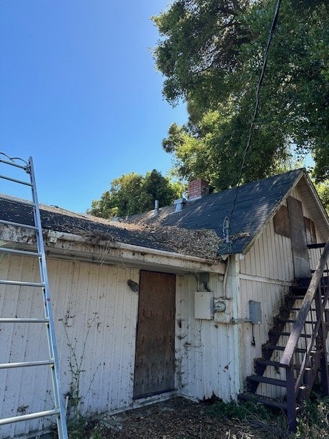 A dilapidated house with a damaged roof, an old staircase, and an overgrown yard.