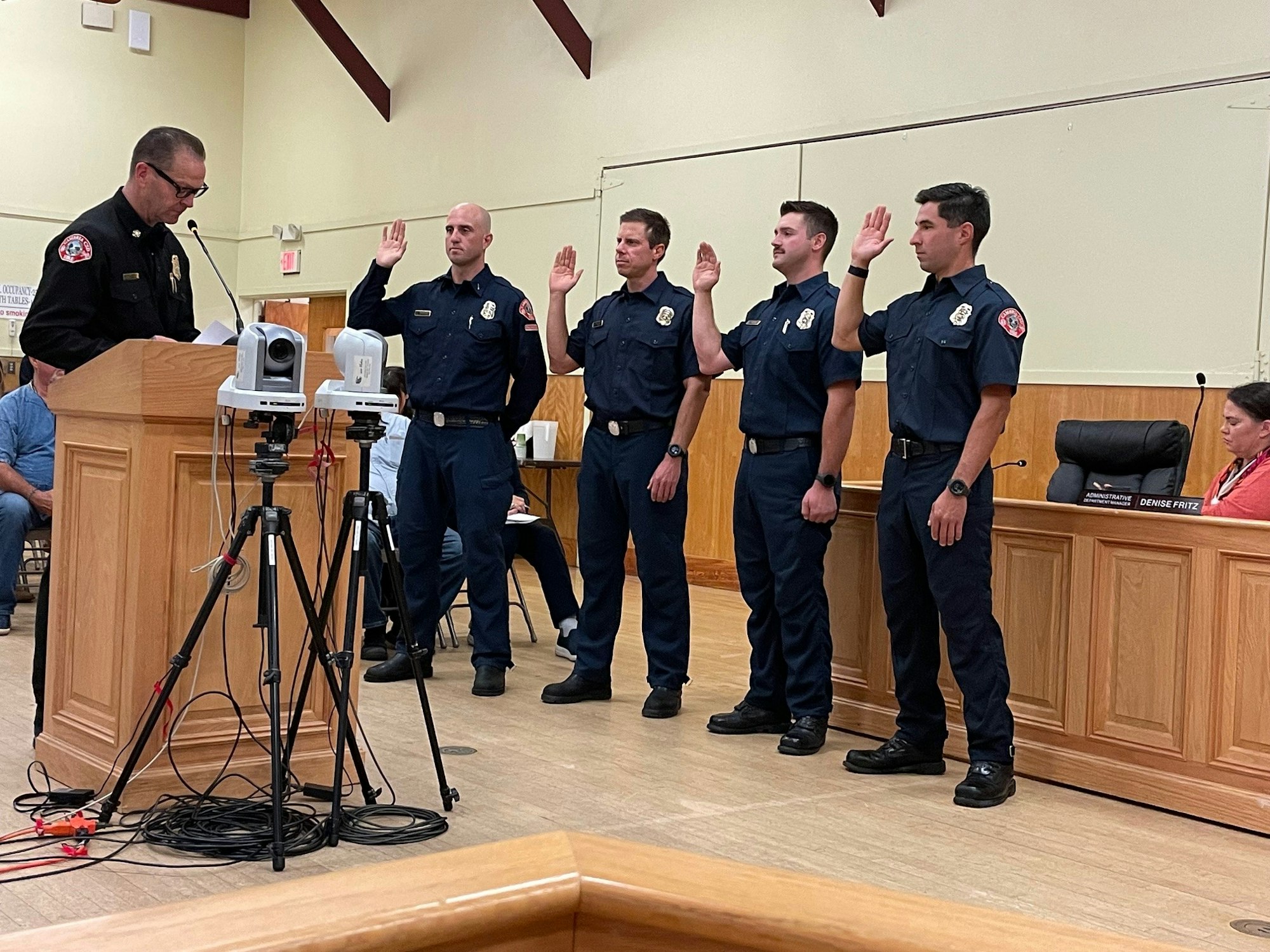 A group of firefighters taking an oath, led by an officer, in a formal indoor ceremony.