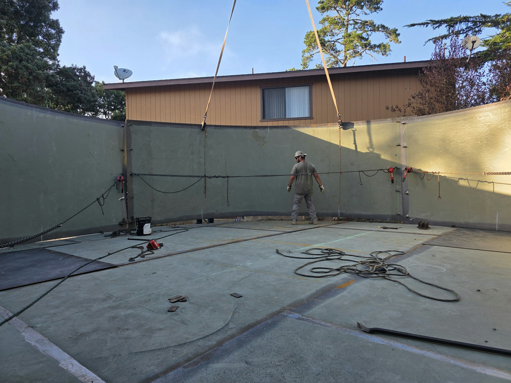 A worker inside a large, partially constructed tank with cables and equipment around.