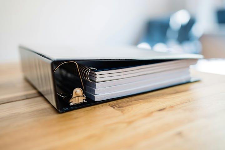 A large, closed ring binder on a wooden surface.