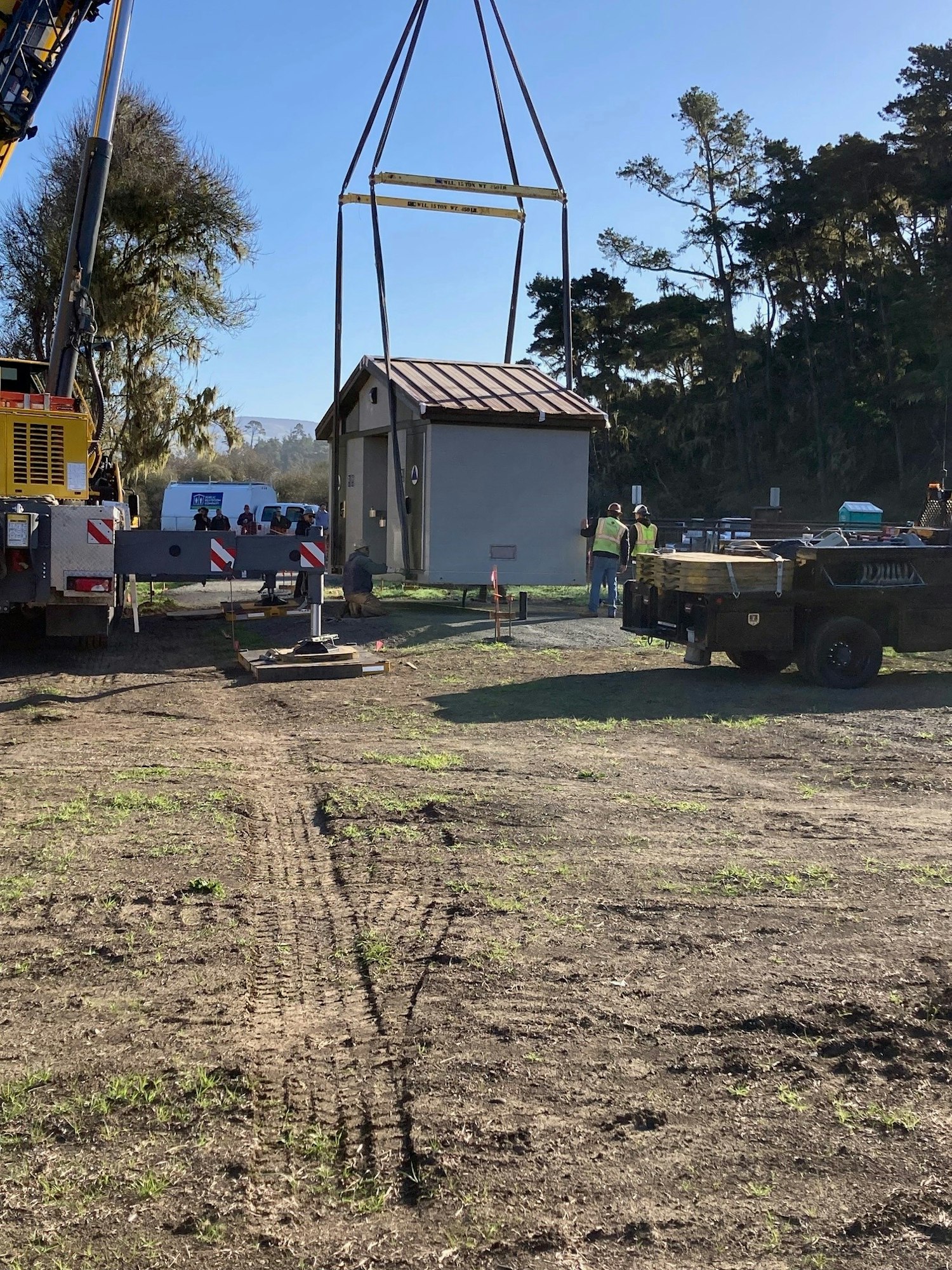 A small building is being lifted by a crane; people in safety vests and machinery are present.