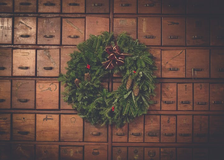 A festive wreath with pinecones and a bow hangs on a wall of vintage wooden drawers.
