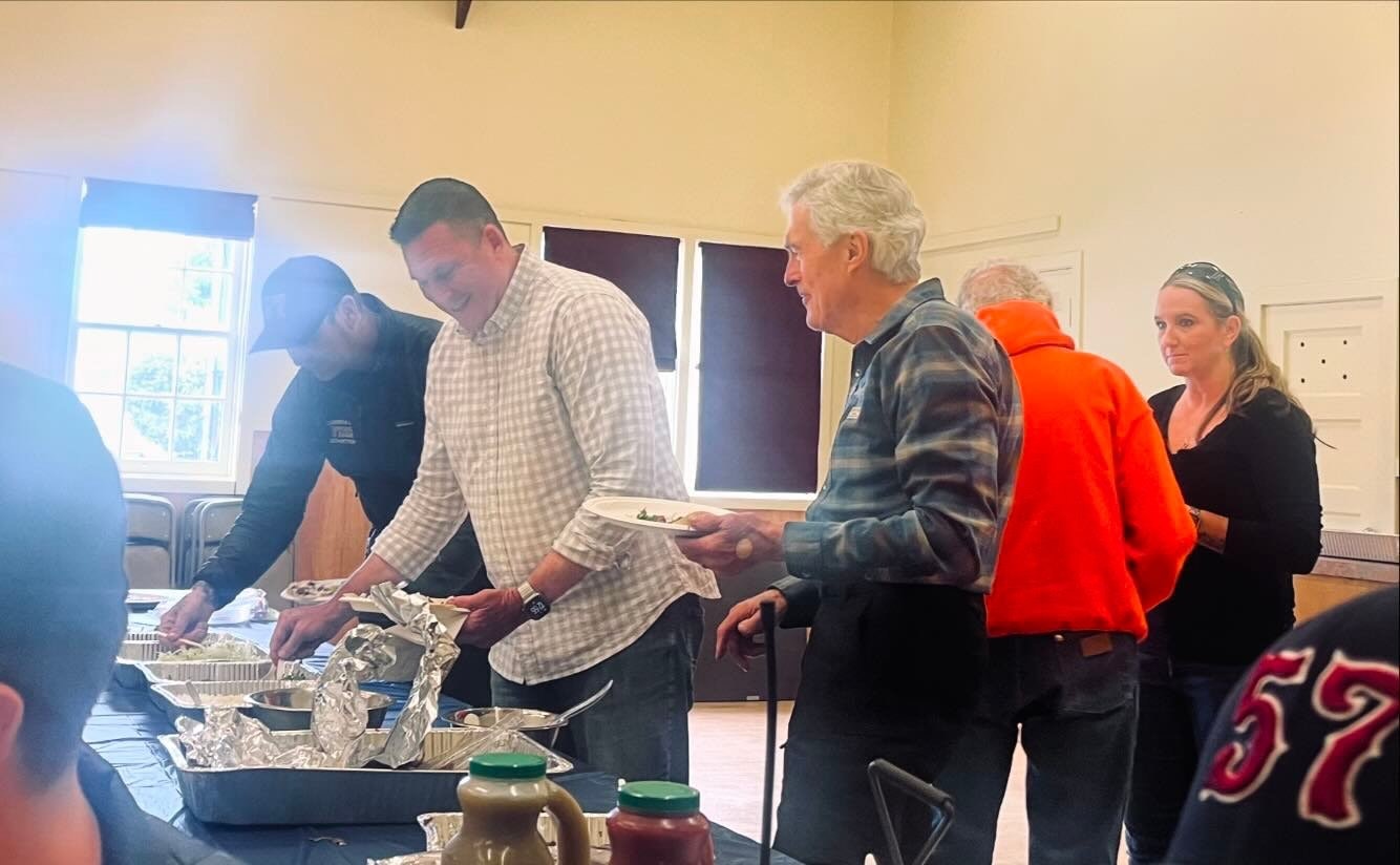 People serving food at a buffet in a community hall.