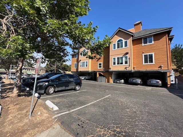 Orange multi-story building with undercroft parking, cars, trees, and a clear sky.