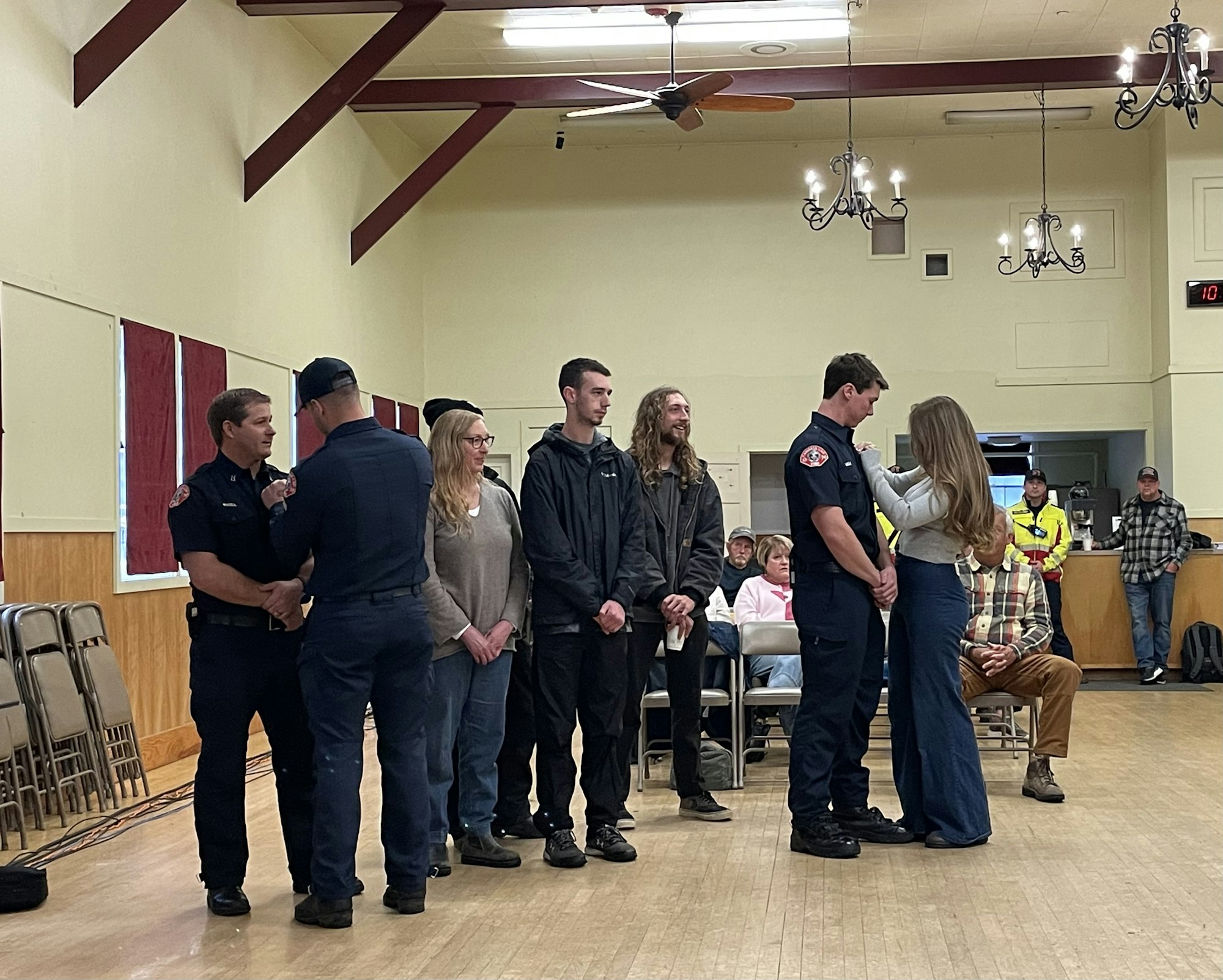 People in a room, including individuals in uniforms, lined up in a ceremony or event. Some are placing pins on others.