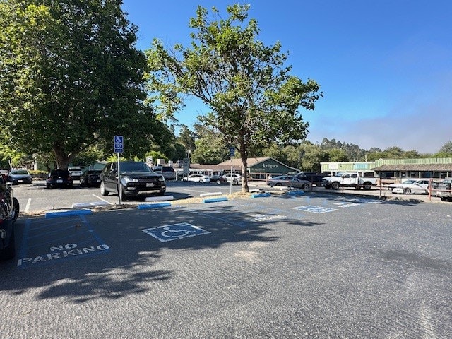 A parking lot with cars, trees, handicap parking spaces, and a clear blue sky.