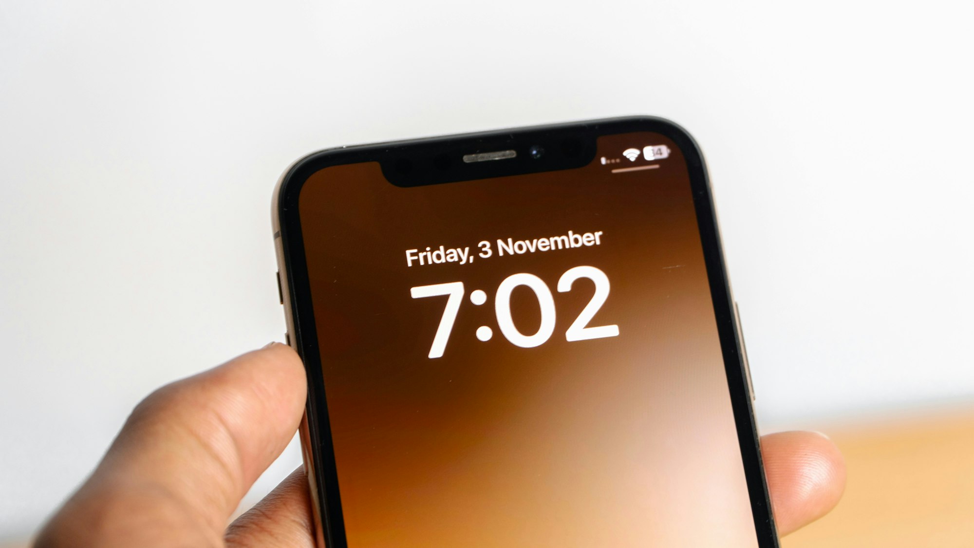 A hand holding a smartphone displaying the time 7:02 and the date Friday, 3 November.