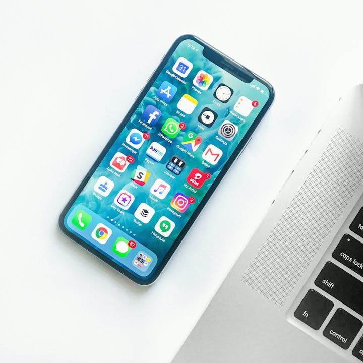 A smartphone with various app icons on the home screen next to a laptop on a white surface.