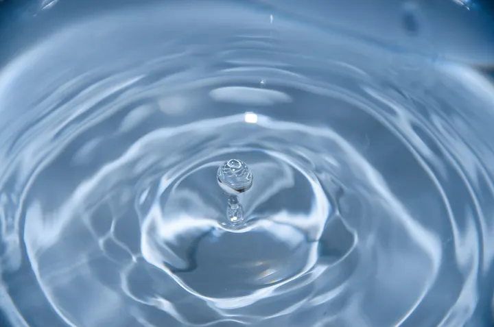 A close-up photo capturing a water droplet impact, creating ripples and a suspended droplet.