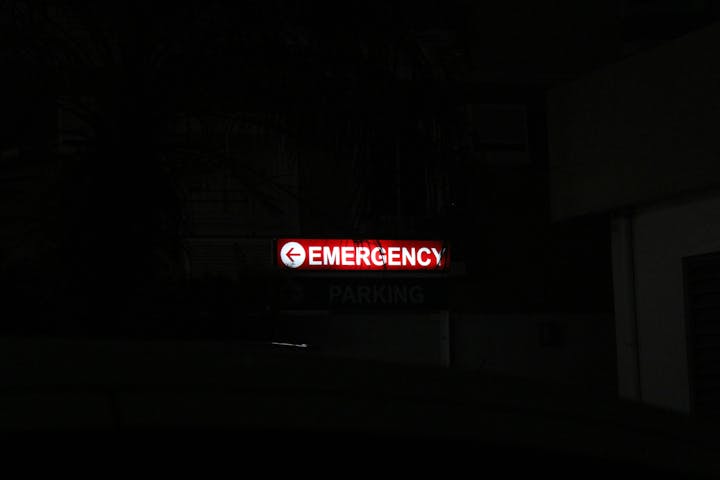 A dimly lit "EMERGENCY" sign with an arrow pointing left, partially obscured by shadows.