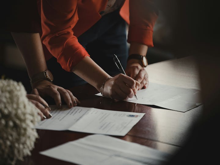 A person in a red sleeve is signing documents on a wooden table.