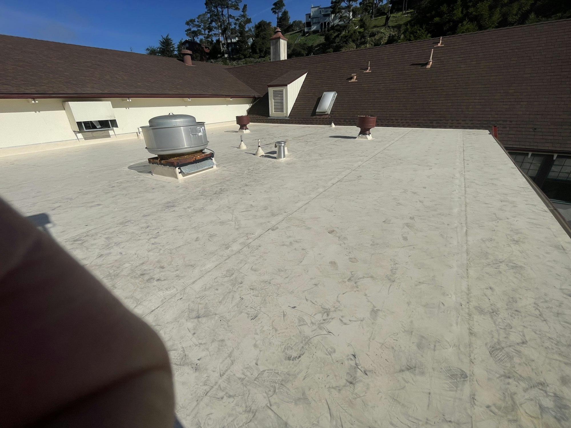 The image shows a flat rooftop with a large silver unit, vents, and sloped roofs in the background. Clear sky above.