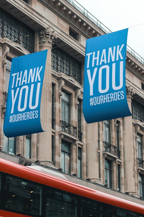 Blue banners saying “Thank You #OurHeroes” outside a building with columns, with a red bus passing by.