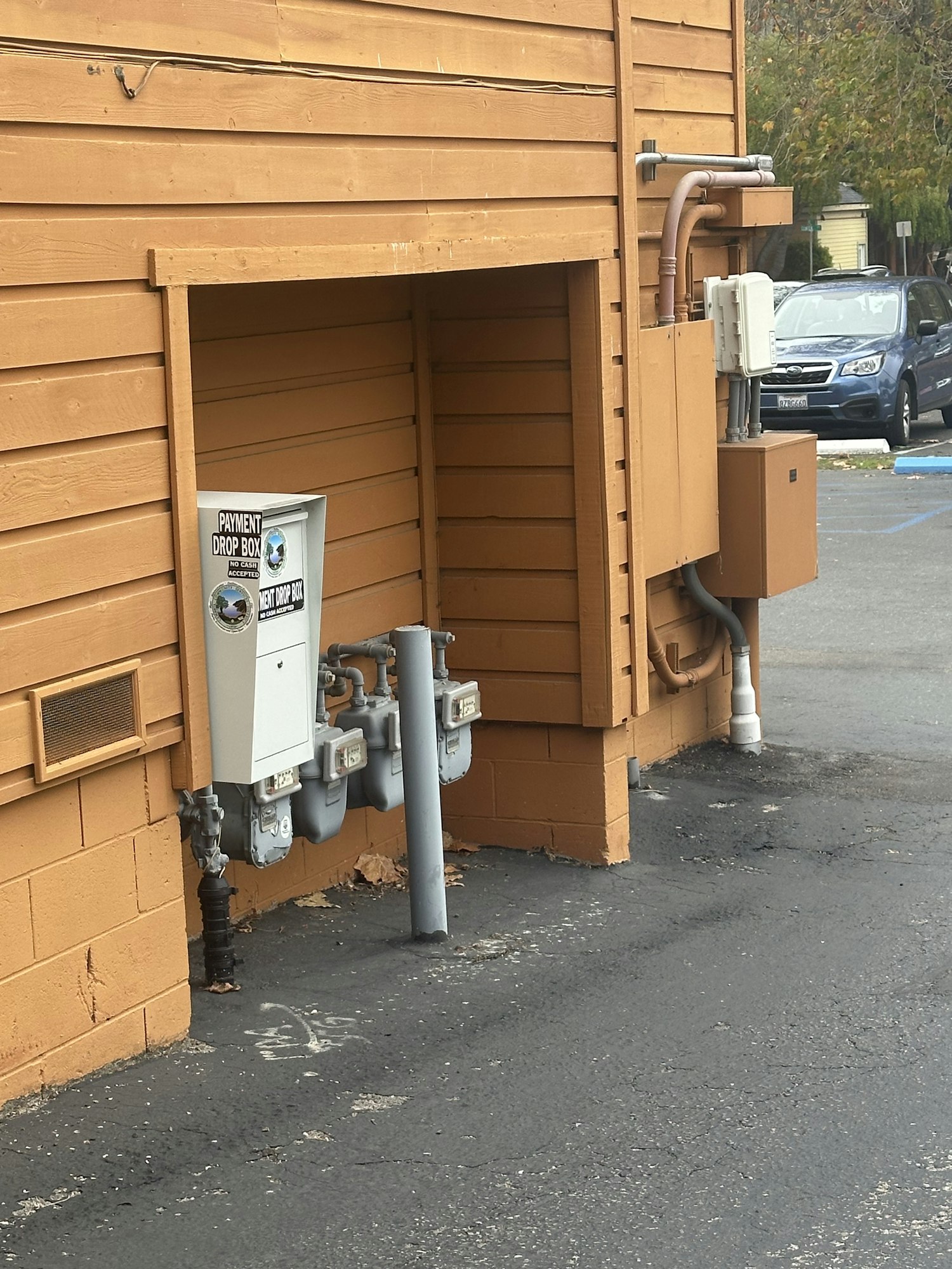 Wooden building exterior with utility meters, pipes, and a "Payment Drop Box."