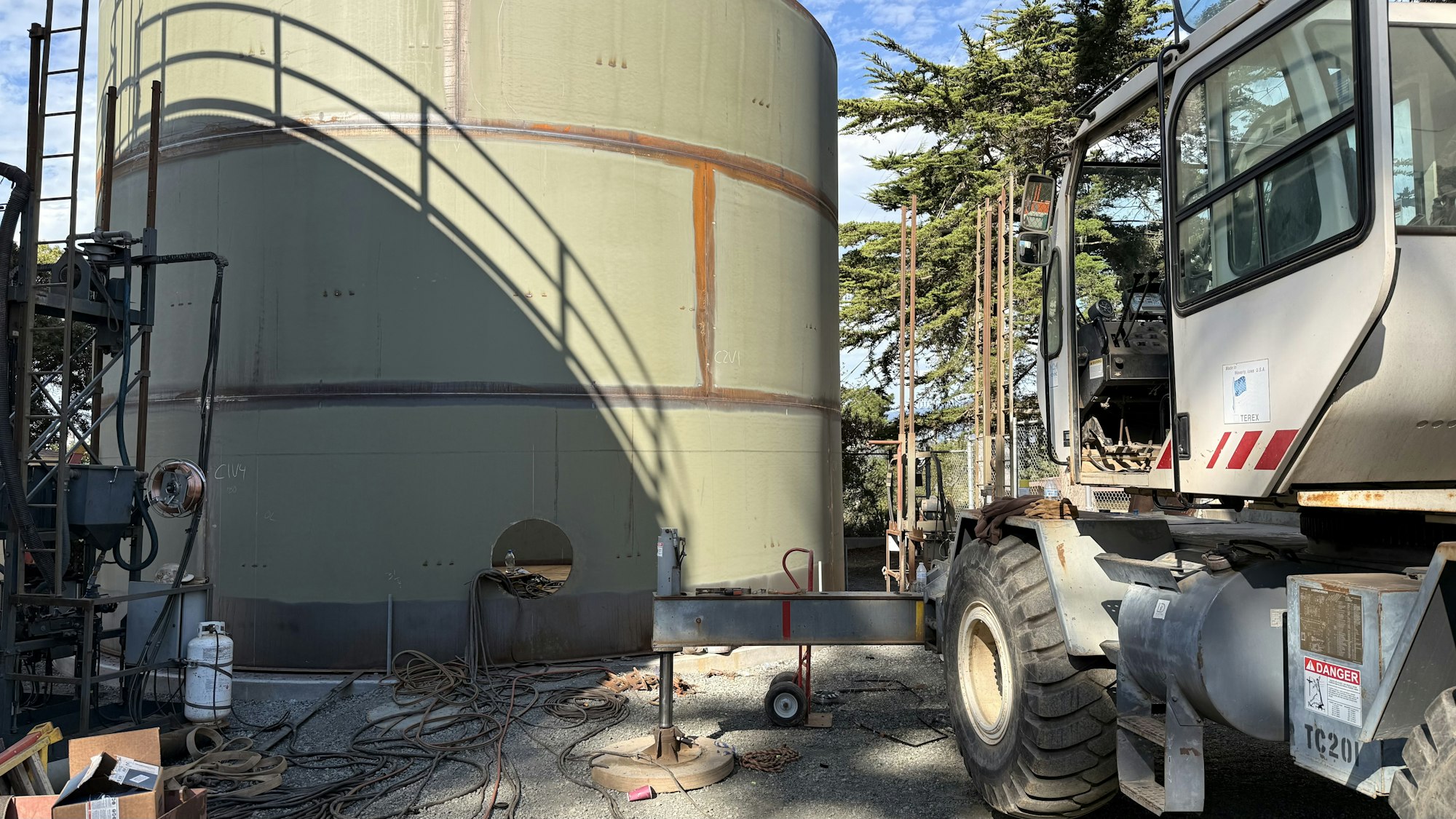 A large industrial tank with equipment near it, and a construction vehicle on the right.