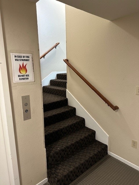 Staircase with handrails, fire safety sign, and an elevator call button.