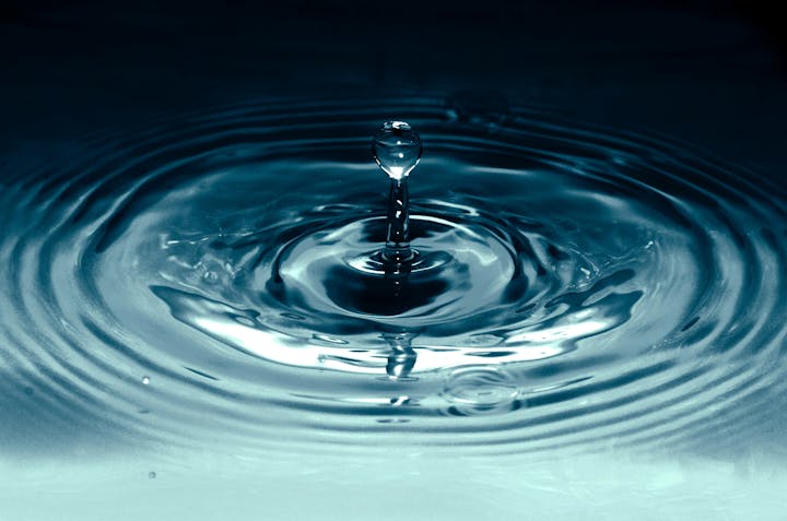 A close-up of a water droplet creating ripples in a calm blue surface.